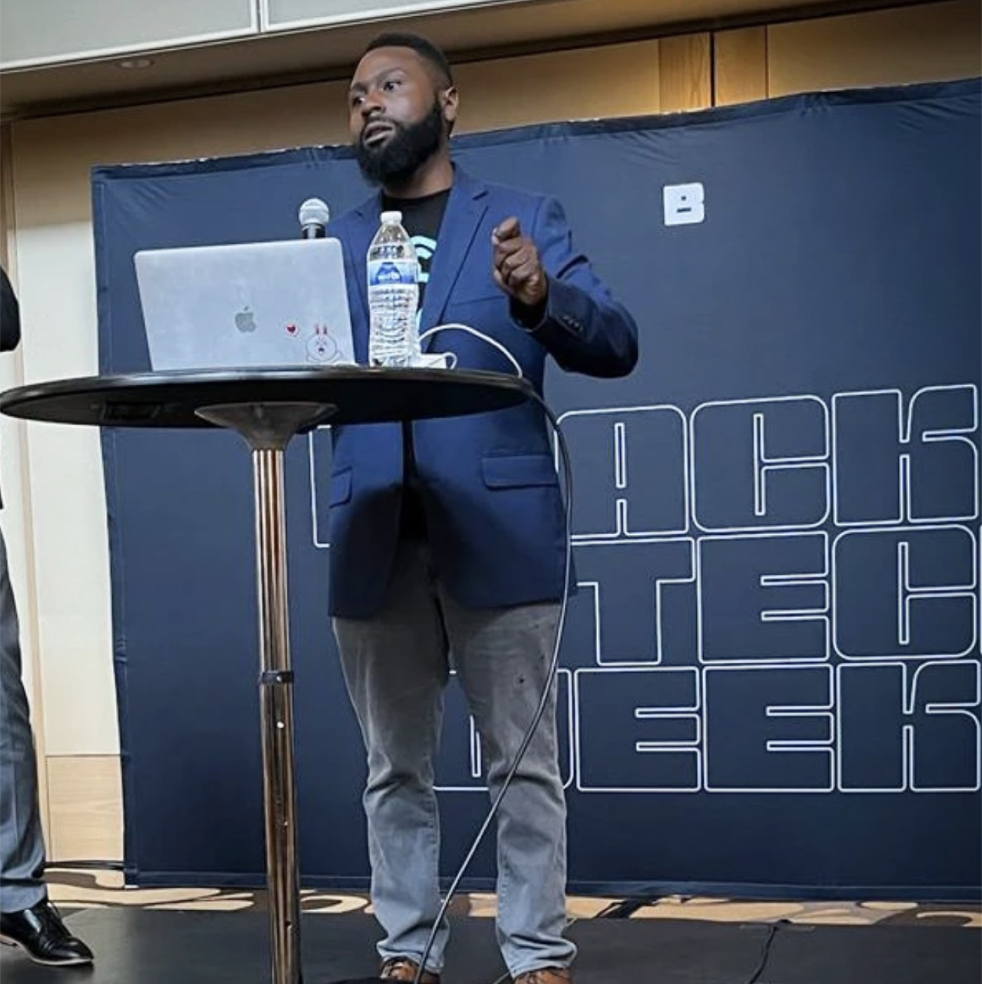 Manny speaking onstage beside a laptop and microphone