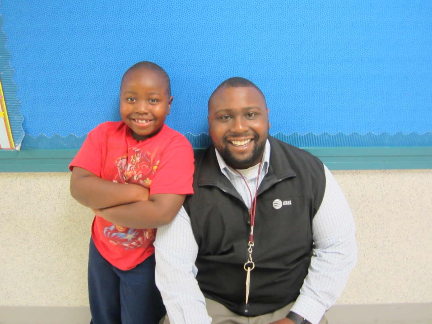 Manny smiling beside a young student in a classroom